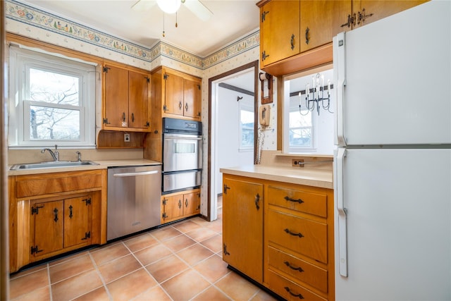 kitchen with appliances with stainless steel finishes, brown cabinets, light countertops, a sink, and a warming drawer