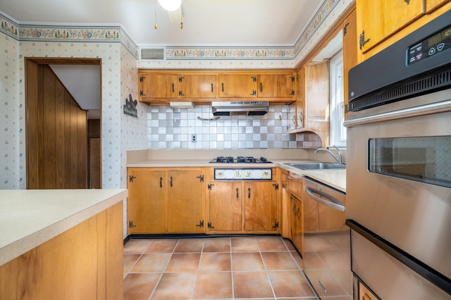 kitchen featuring under cabinet range hood, stainless steel appliances, a sink, light countertops, and wallpapered walls