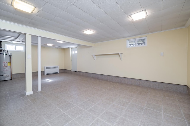 basement featuring water heater, light tile patterned floors, and radiator heating unit