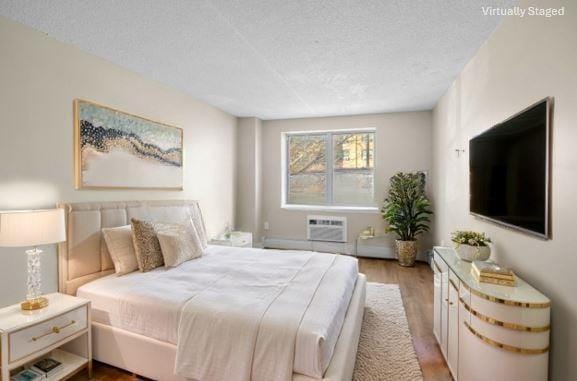 bedroom with wood finished floors, a textured ceiling, and a wall mounted air conditioner