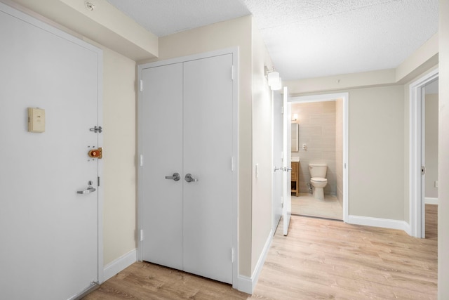 foyer with baseboards, a textured ceiling, and light wood finished floors