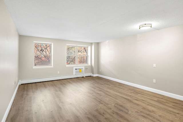 unfurnished room featuring baseboards, a wall unit AC, wood finished floors, a textured ceiling, and a baseboard heating unit