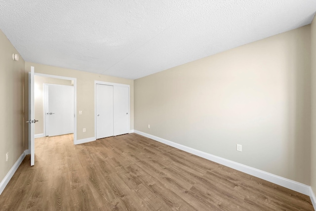 unfurnished bedroom with a closet, a textured ceiling, baseboards, and wood finished floors