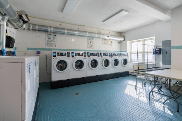 shared laundry area with electric panel, washer and clothes dryer, and a textured ceiling