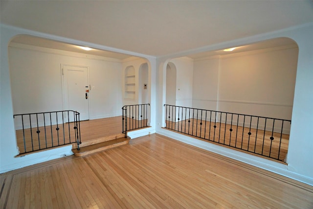 empty room featuring arched walkways, hardwood / wood-style flooring, and built in features