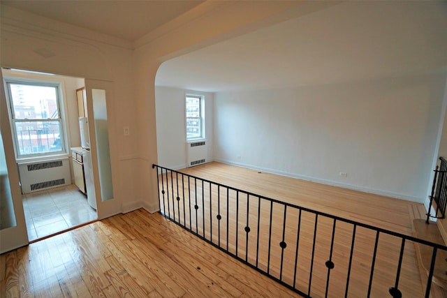 unfurnished room with radiator, baseboards, arched walkways, and wood finished floors