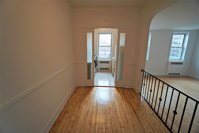 hallway with light wood-style floors, a wealth of natural light, and radiator