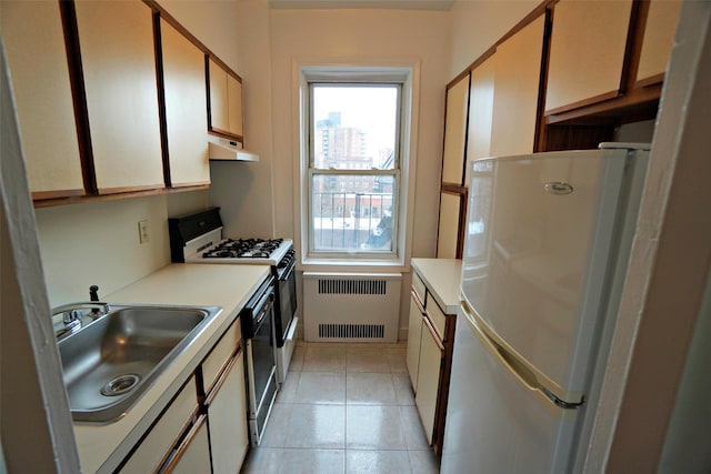 kitchen featuring radiator, freestanding refrigerator, gas range oven, a sink, and exhaust hood