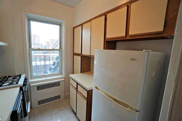 kitchen featuring light tile patterned floors, radiator, freestanding refrigerator, light countertops, and stainless steel range with gas cooktop