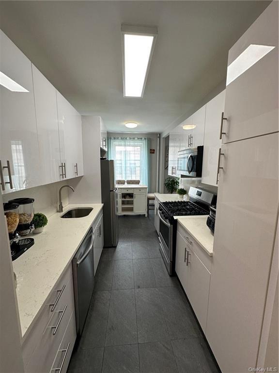 kitchen with stainless steel appliances, dark tile patterned flooring, a sink, white cabinets, and light stone countertops