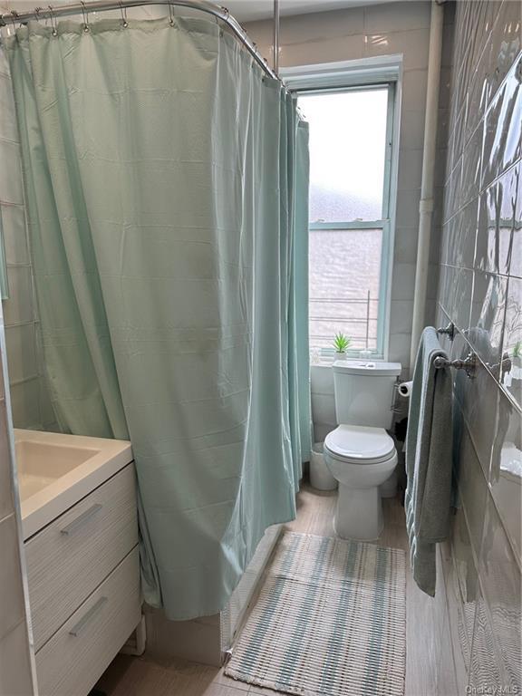 full bath with toilet, tile walls, and vanity