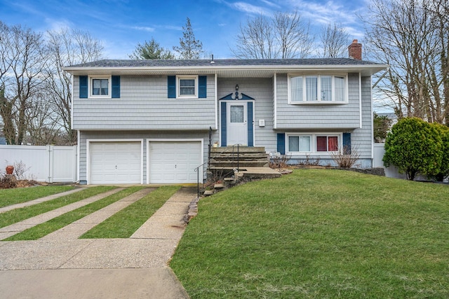 split foyer home with a chimney, concrete driveway, an attached garage, a front yard, and fence