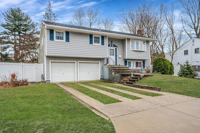 bi-level home featuring driveway, a chimney, an attached garage, fence, and a front lawn