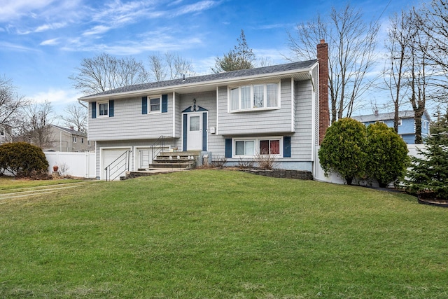 bi-level home with an attached garage, a chimney, fence, and a front lawn