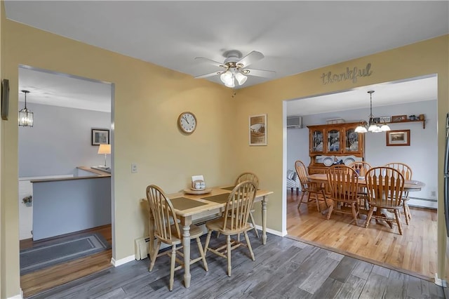 dining space featuring ceiling fan with notable chandelier, baseboards, baseboard heating, and wood finished floors