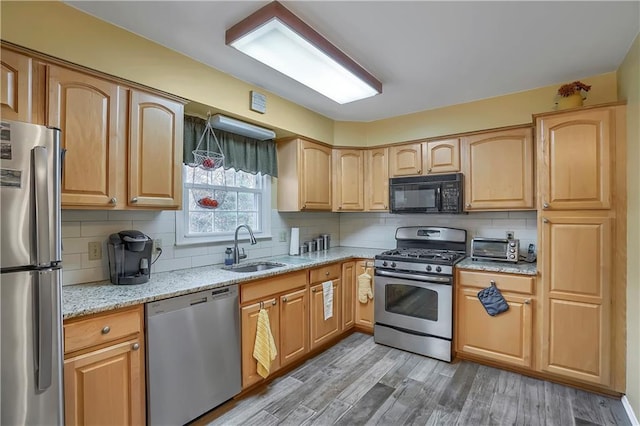 kitchen with light wood finished floors, a sink, light stone countertops, stainless steel appliances, and backsplash