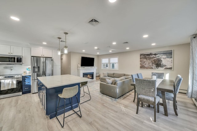 kitchen with light stone counters, stainless steel appliances, visible vents, white cabinets, and a glass covered fireplace