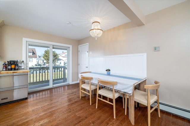 dining space with a chandelier, a wainscoted wall, a baseboard heating unit, and wood finished floors