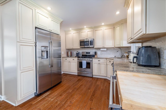 kitchen with dark wood-type flooring, appliances with stainless steel finishes, decorative backsplash, and a sink