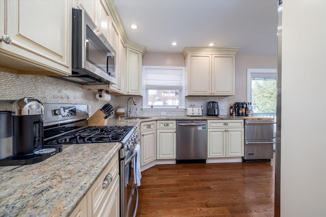 kitchen featuring light stone counters, stainless steel appliances, dark wood-style flooring, a sink, and decorative backsplash