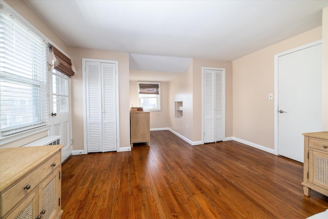 unfurnished bedroom with dark wood-style floors, baseboards, and multiple closets