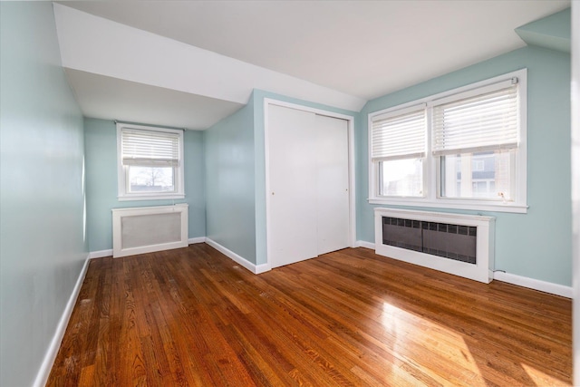 additional living space with baseboards, a fireplace, wood finished floors, and radiator