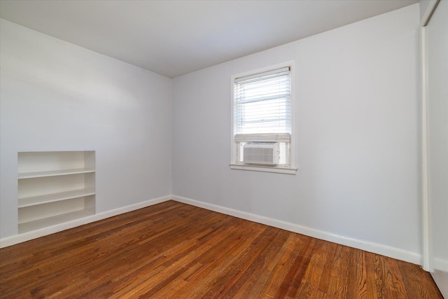 spare room with built in features, cooling unit, baseboards, and wood finished floors