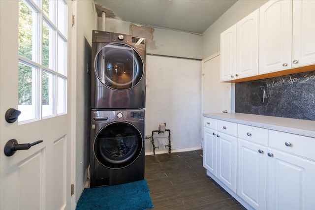 laundry area featuring stacked washer / drying machine, dark wood finished floors, cabinet space, and plenty of natural light