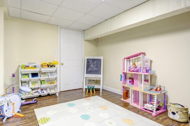 recreation room featuring a paneled ceiling, baseboards, and wood finished floors