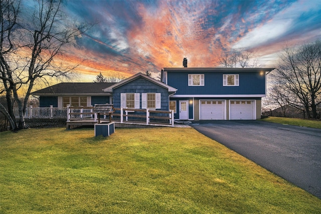 tri-level home with a wooden deck, driveway, an attached garage, and a yard