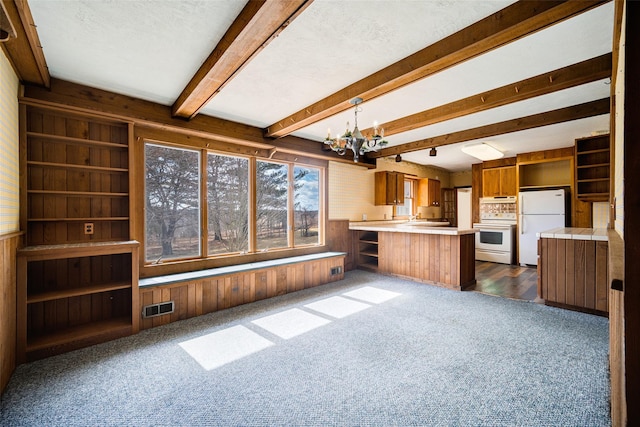 kitchen with white appliances, brown cabinetry, visible vents, wood walls, and a notable chandelier