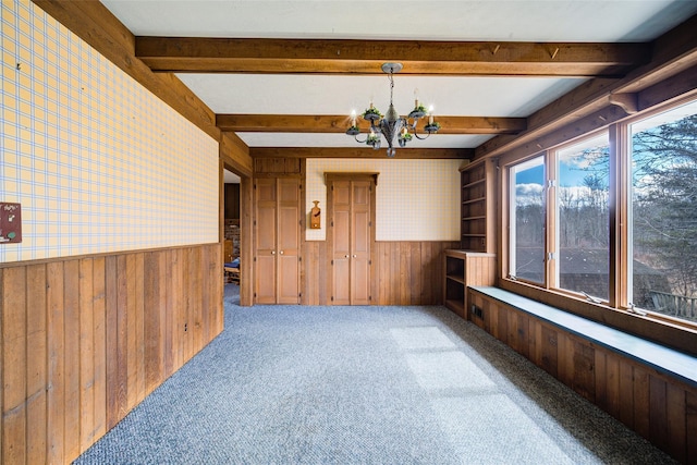 carpeted spare room featuring a wainscoted wall, wallpapered walls, wood walls, beamed ceiling, and a notable chandelier