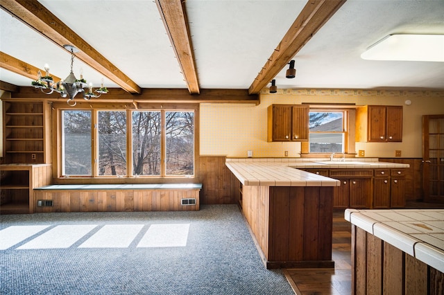 kitchen featuring beamed ceiling, brown cabinets, a sink, tile counters, and a chandelier