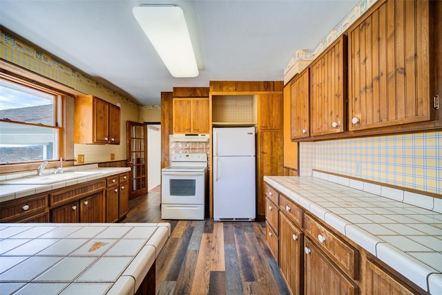 kitchen featuring under cabinet range hood, tile countertops, white appliances, and brown cabinetry