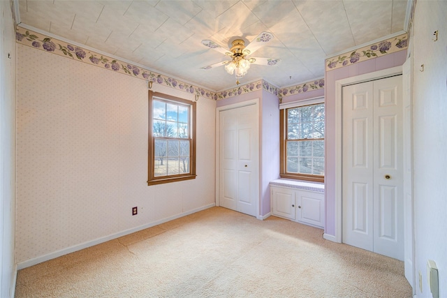 unfurnished bedroom featuring multiple windows, multiple closets, light carpet, and wallpapered walls