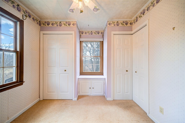 unfurnished bedroom with baseboards, wallpapered walls, multiple closets, light carpet, and crown molding