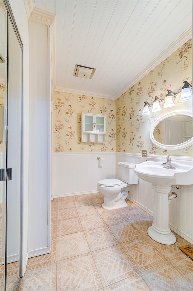 bathroom featuring tile patterned flooring, wallpapered walls, crown molding, toilet, and wainscoting