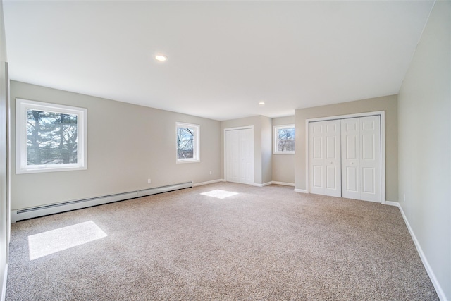 unfurnished bedroom featuring baseboards, recessed lighting, multiple closets, a baseboard heating unit, and carpet flooring