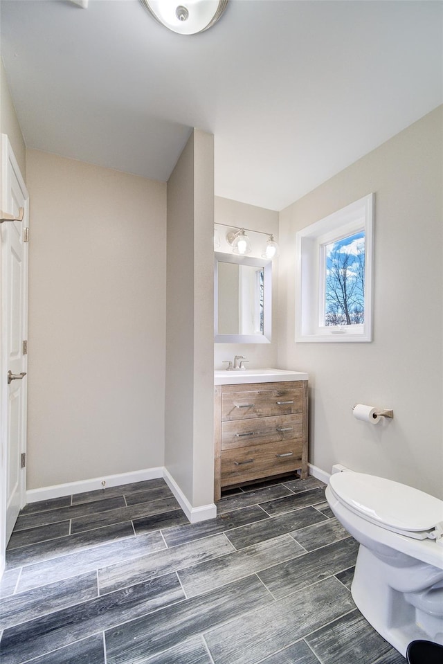 half bathroom featuring wood finish floors, baseboards, toilet, and vanity