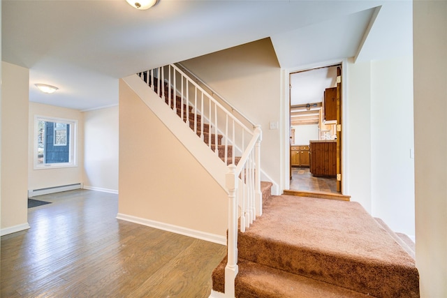 stairway featuring a baseboard heating unit, baseboards, and wood finished floors