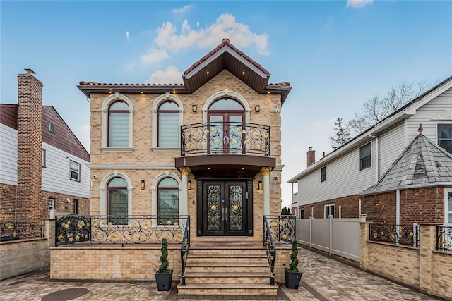 view of front facade featuring a balcony, brick siding, fence, and french doors