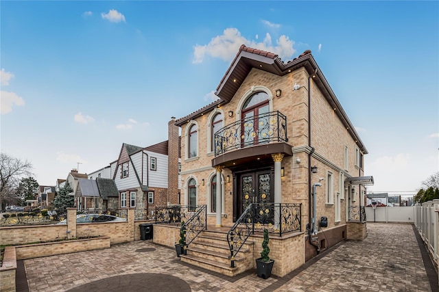 view of front of house with french doors, a tile roof, a patio area, fence, and a balcony