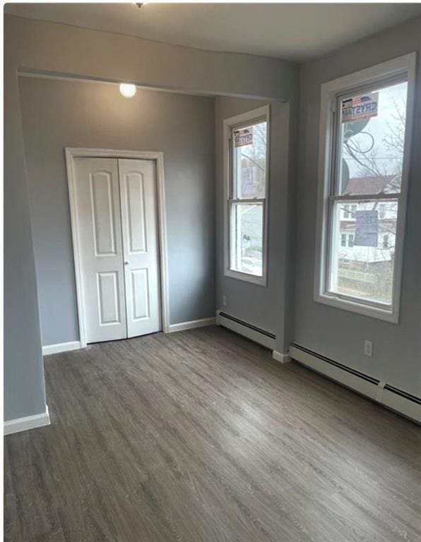 unfurnished bedroom with a baseboard radiator, a closet, baseboards, and wood finished floors