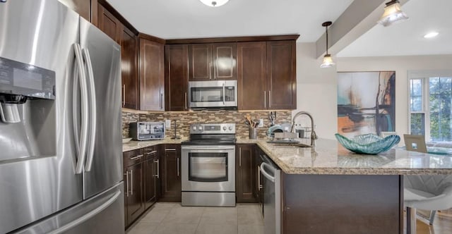 kitchen featuring light stone counters, stainless steel appliances, a peninsula, a sink, and tasteful backsplash