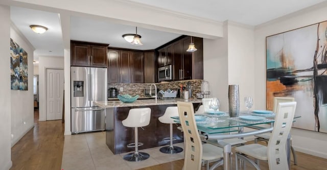 kitchen featuring dark brown cabinetry, decorative backsplash, a breakfast bar area, light stone counters, and stainless steel appliances