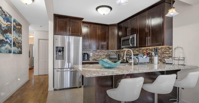 kitchen featuring dark brown cabinetry, light stone counters, stainless steel appliances, and a sink