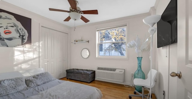 bedroom with a closet, a wall mounted air conditioner, ceiling fan, and wood finished floors