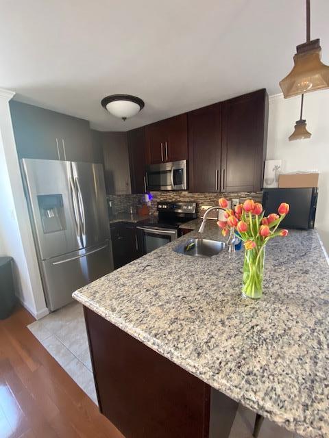 kitchen with tasteful backsplash, light wood-style flooring, appliances with stainless steel finishes, a sink, and dark brown cabinets