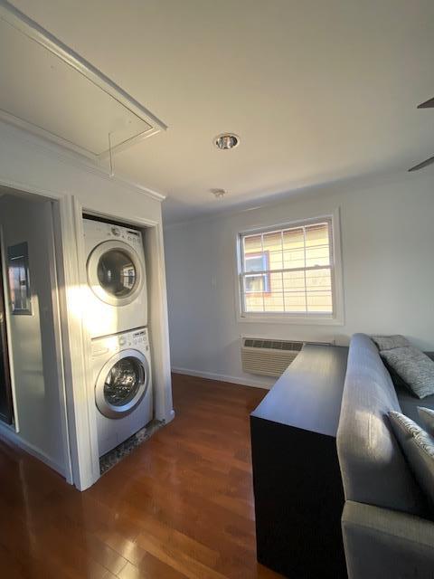 laundry room featuring stacked washer / drying machine, a wall mounted AC, attic access, wood finished floors, and laundry area