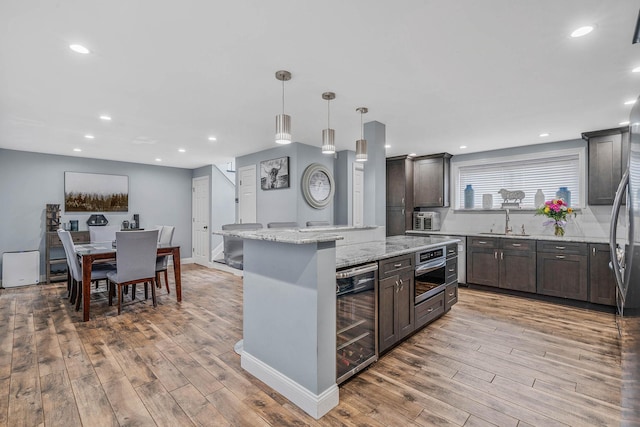 kitchen with light wood-type flooring, a kitchen island, wine cooler, and light stone counters